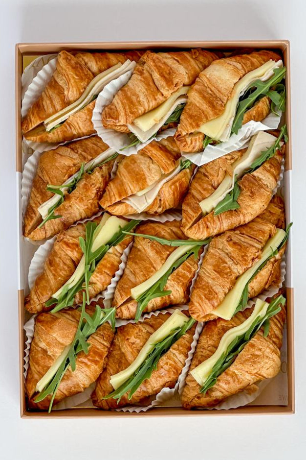 Box of croissant sandwiches with cheese and avocado on a white background