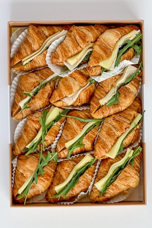 Box of croissant sandwiches with cheese and avocado on a white background